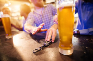 man reaching for car keys with a beer in front of him