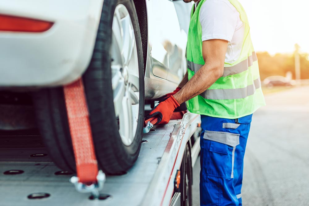 close-up of tow truck driving securing a car on a flatbed