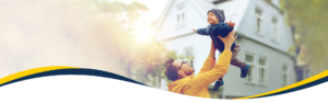 Father lifting his laughing infant son in the air in front of a two-storey home.