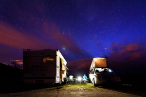 An RV and camper van parked side-by-side under a startlit night