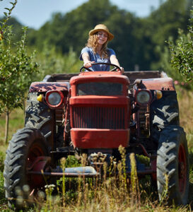 woman riding on a tractor through an apple orchard