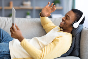 Man relaxing on his couch holding a tablet and wearing earphones