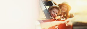 Ypung boy looking out of car window and smiling with mom in background