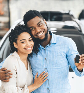 smiling couple holding car keys in front of new car