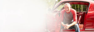 Man sitting in his classic red car looking at camera and smiling