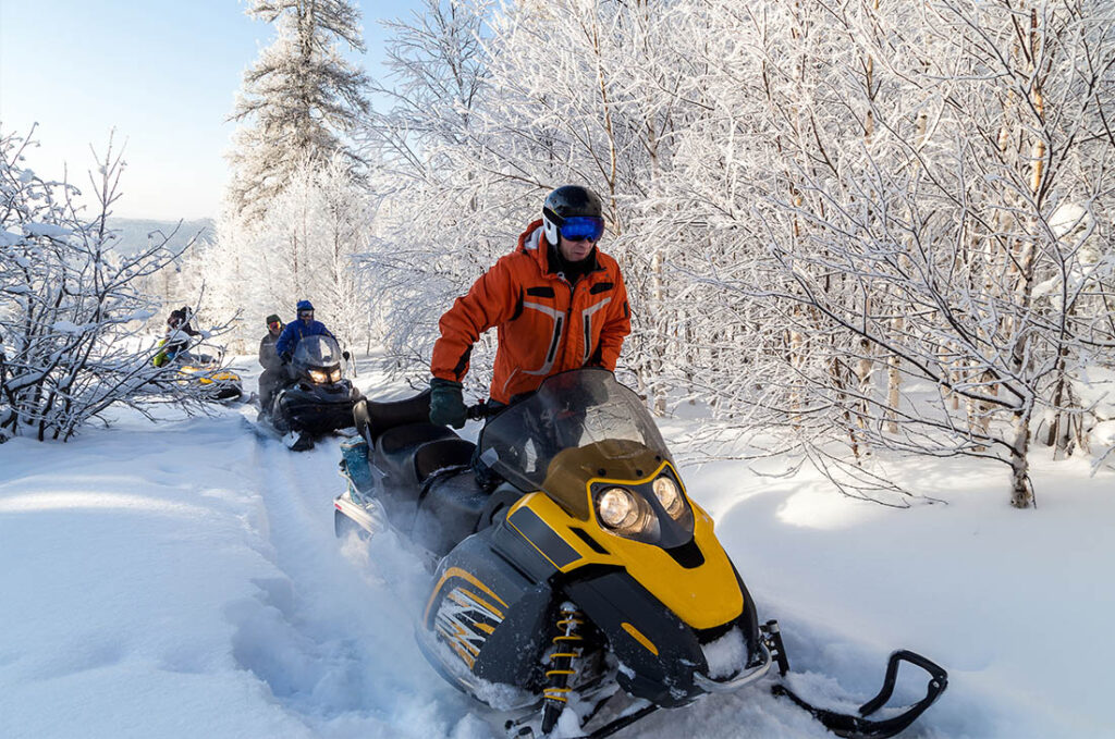 Group of snowmobilers riding through snow covered woods