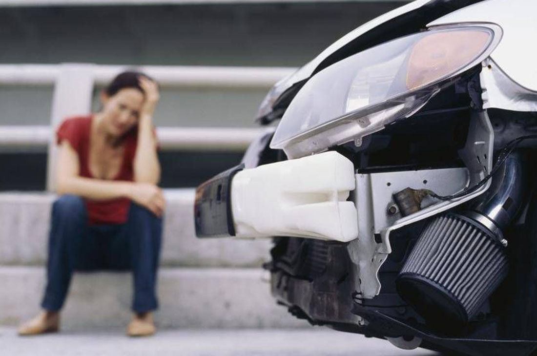 young woman sitting on a curb in front of damaged car