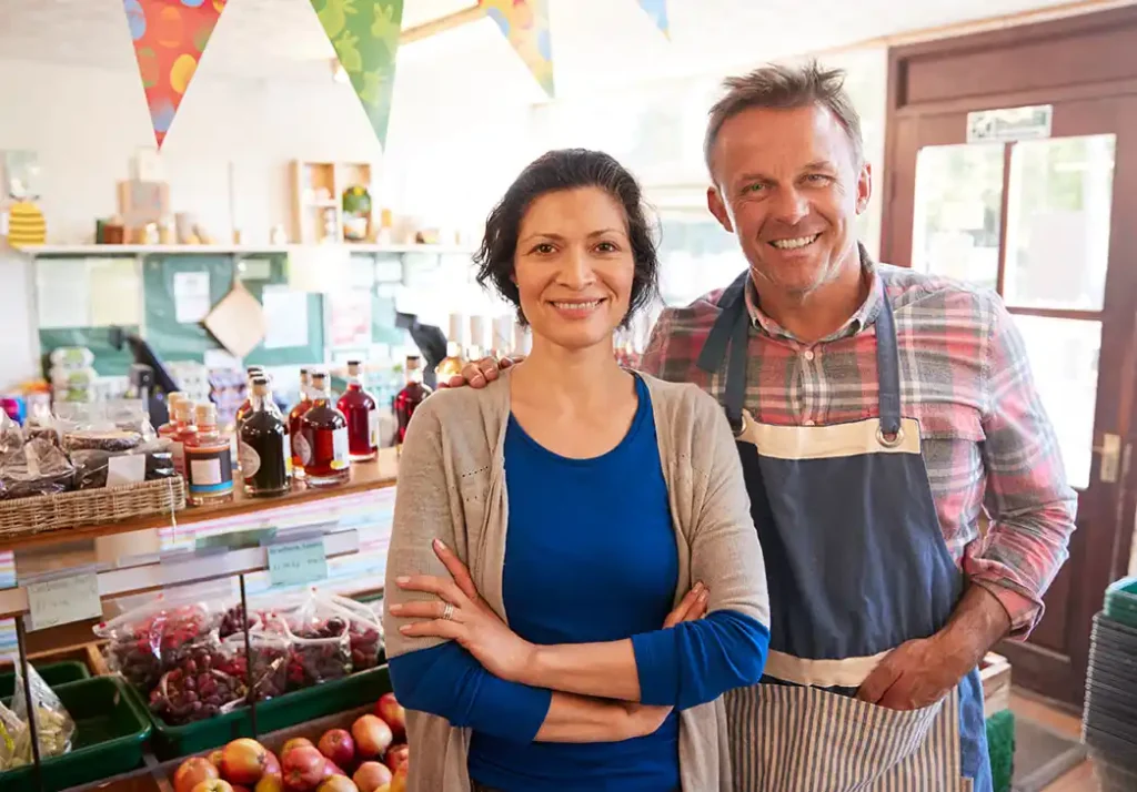 Small business owner couple standing in their variety store and smiling at camera