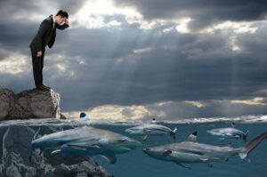 business man standing on a rock looking at sharks swimming at his feet