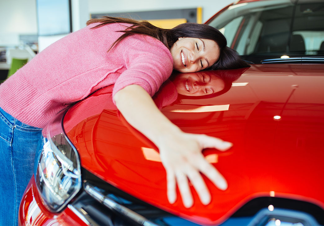 Happy young woman hugging her new red car