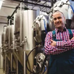 Mature manufacturer standing by storage tank in brewery