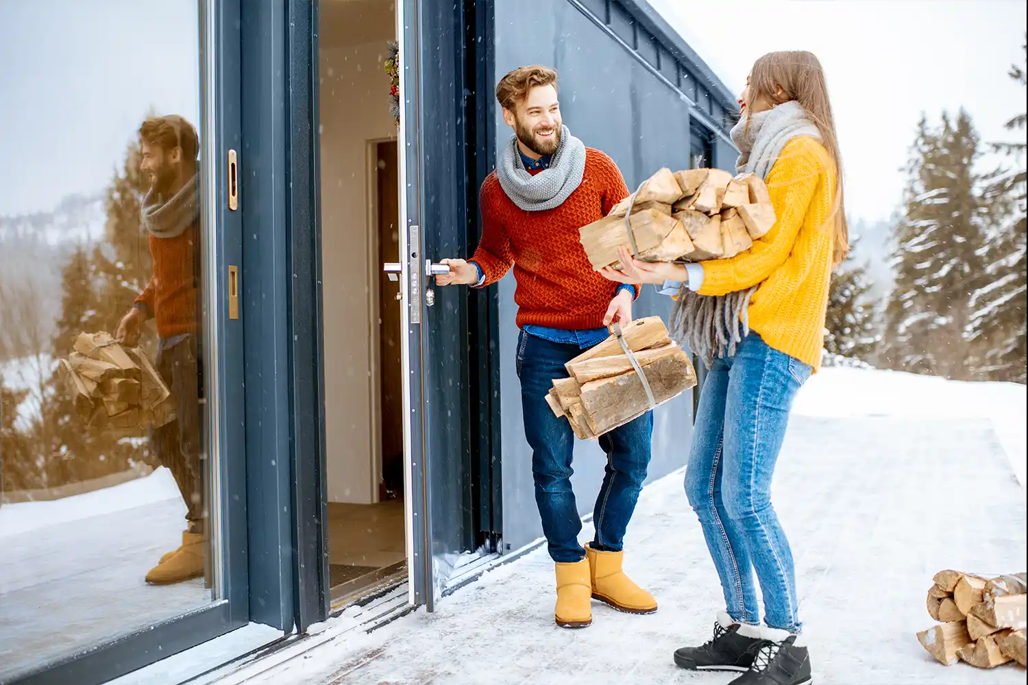 couple dressed in colourful sweaters entering their cottage with firewood during the winter