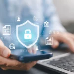 Businessman using smartphone and laptop with shield and padlock icons.